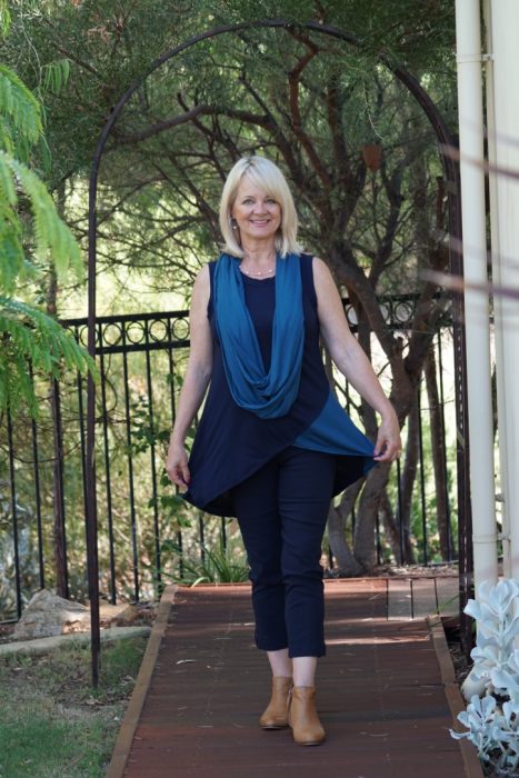 Blonde woman in navy pants and top with a long loop lighter blue scarf.