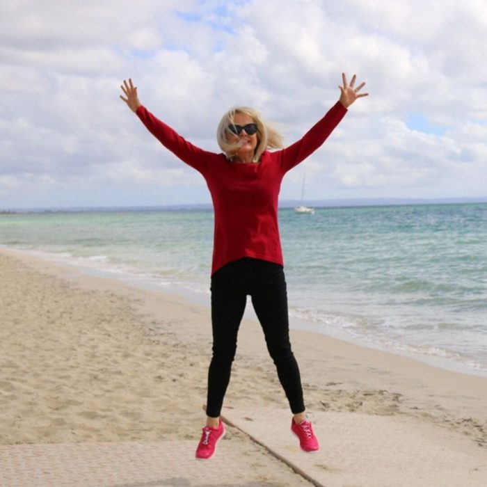 Woman jumping for joy, fully clothed, on beach