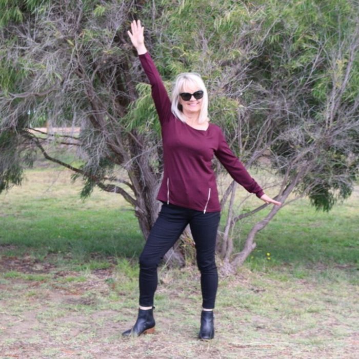 Woman in forest setting wearing black jeans and maroon top.