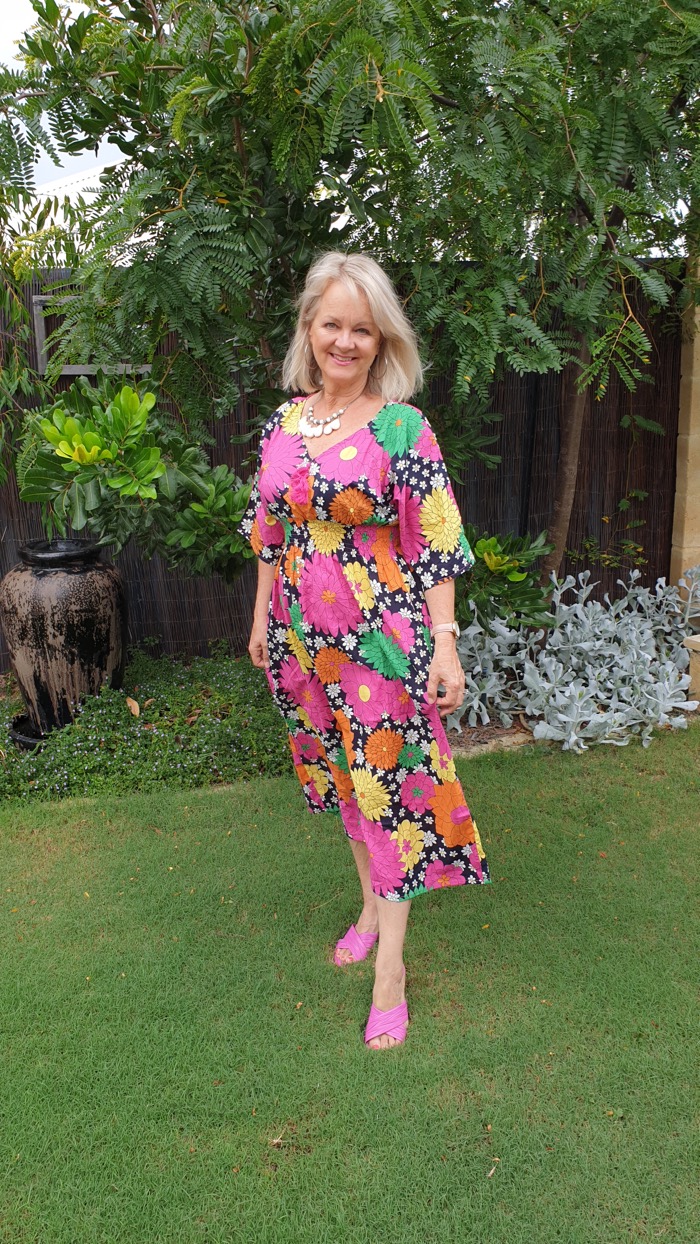 Woman in garden setting wearing a flowery summer dress that could be worn at any event requiring 'resort wear'.