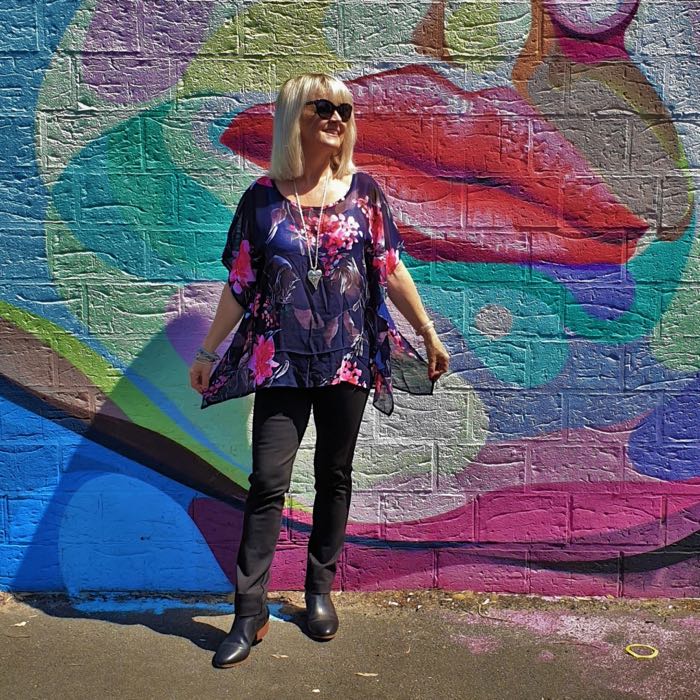 Blonde woman in navy top with flowers. Black trousers and black boots.