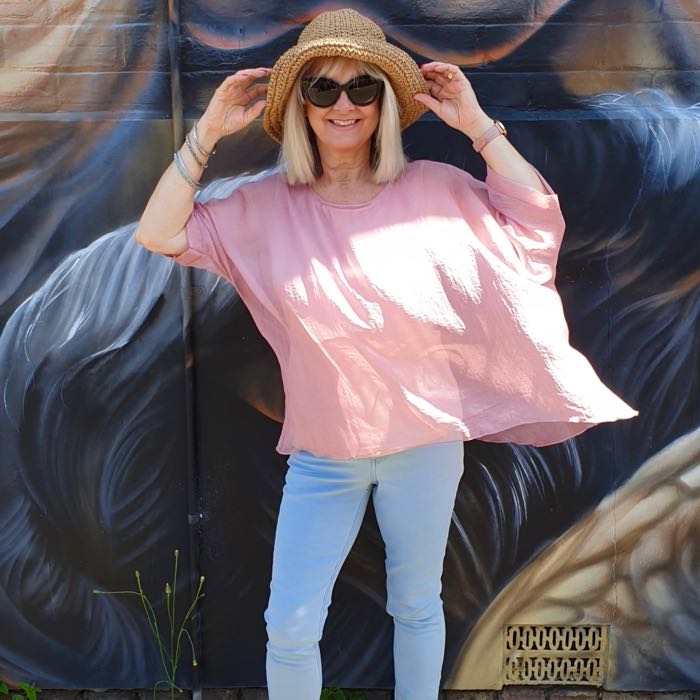 Woman wearing straw hat, black sunglasses, pink flowing top and blue jeans, illustrating a point about how to dress well if you are short.