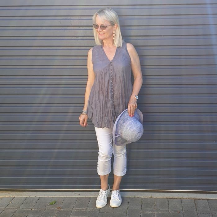 Blonde woman in grey v-neck blouse, white capri pants and white sneakers, illustrating how to dress well if you are short.
