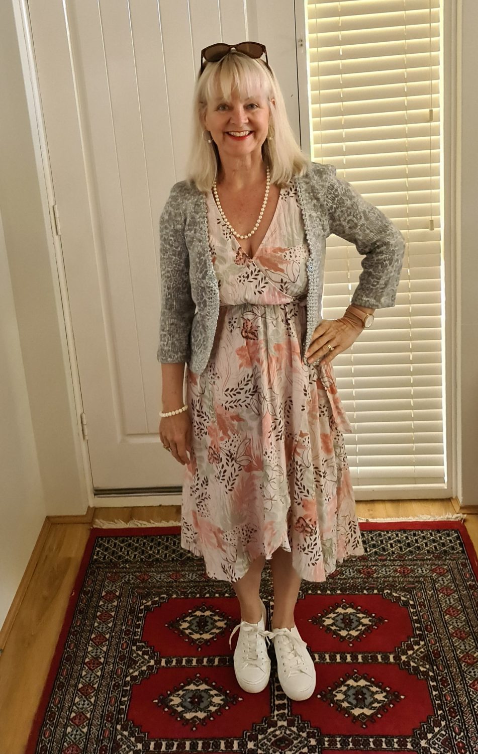 Blond woman in midi dress and grey cardigan standing in front of a white door.