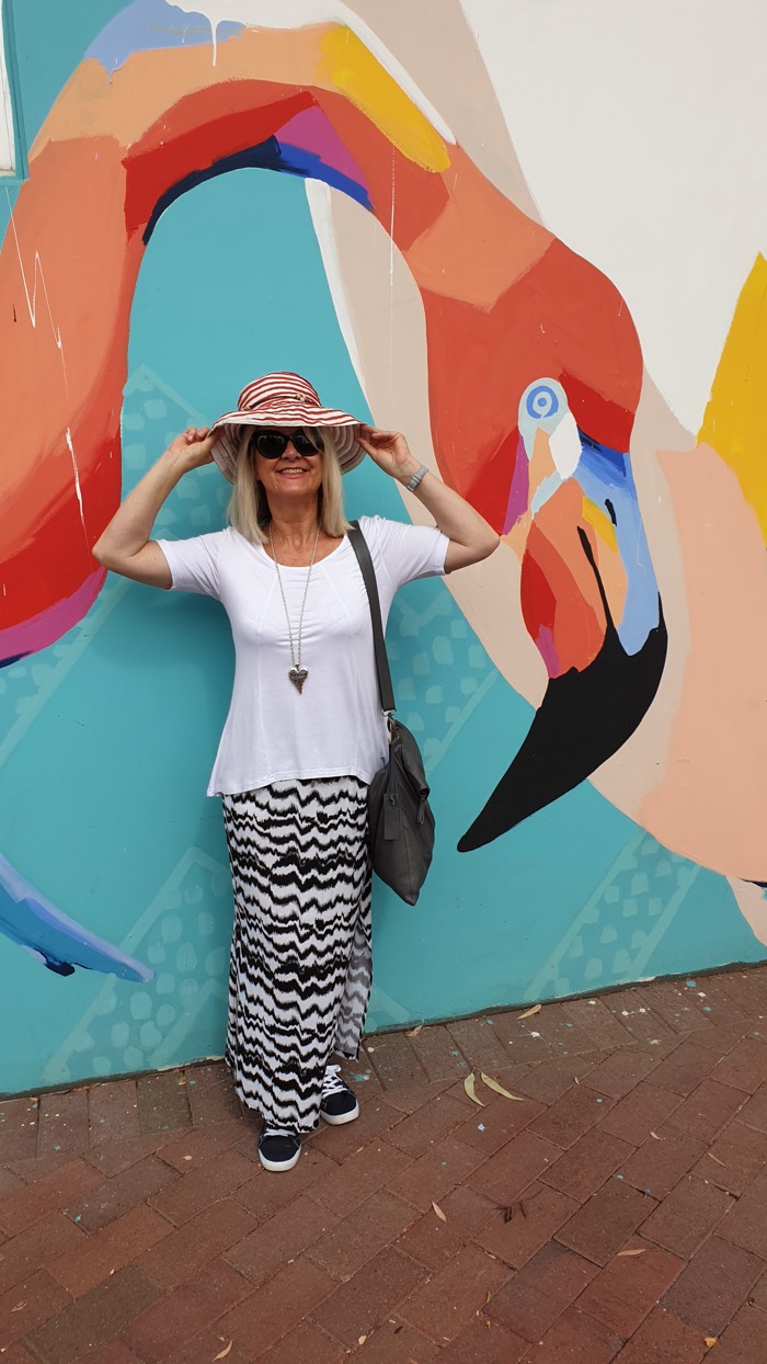 Blond woman in white T and  black and white maxi skirt in front of a colourful mural. Illustrating a point about how to style maxi skirts without looking frumpy.
