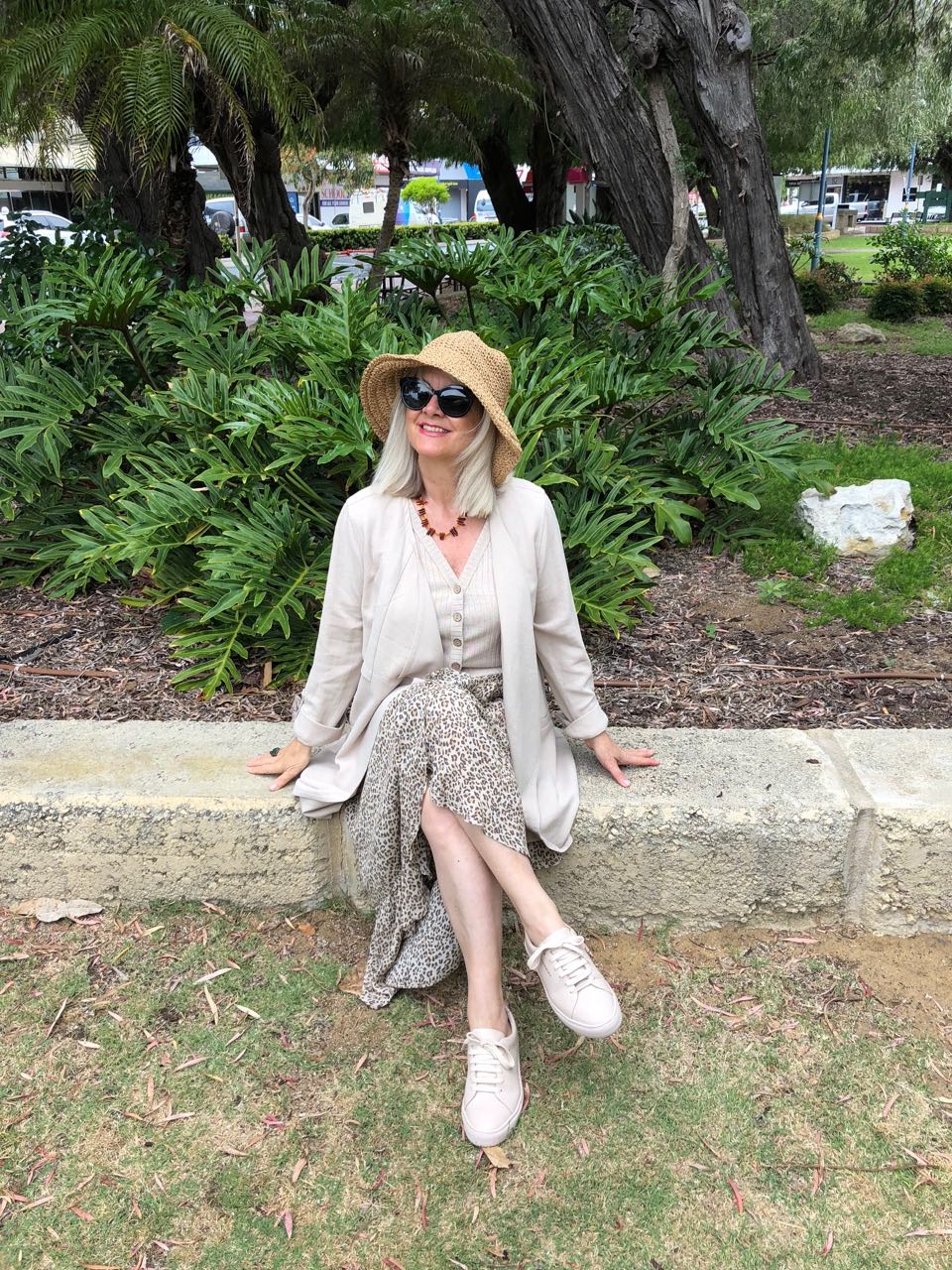 Blond woman in straw hat wearing animal print long skirt, oatmeal top and jacket and sneakers illustrating a point in the post how to wear long skirts without looking frumpy.