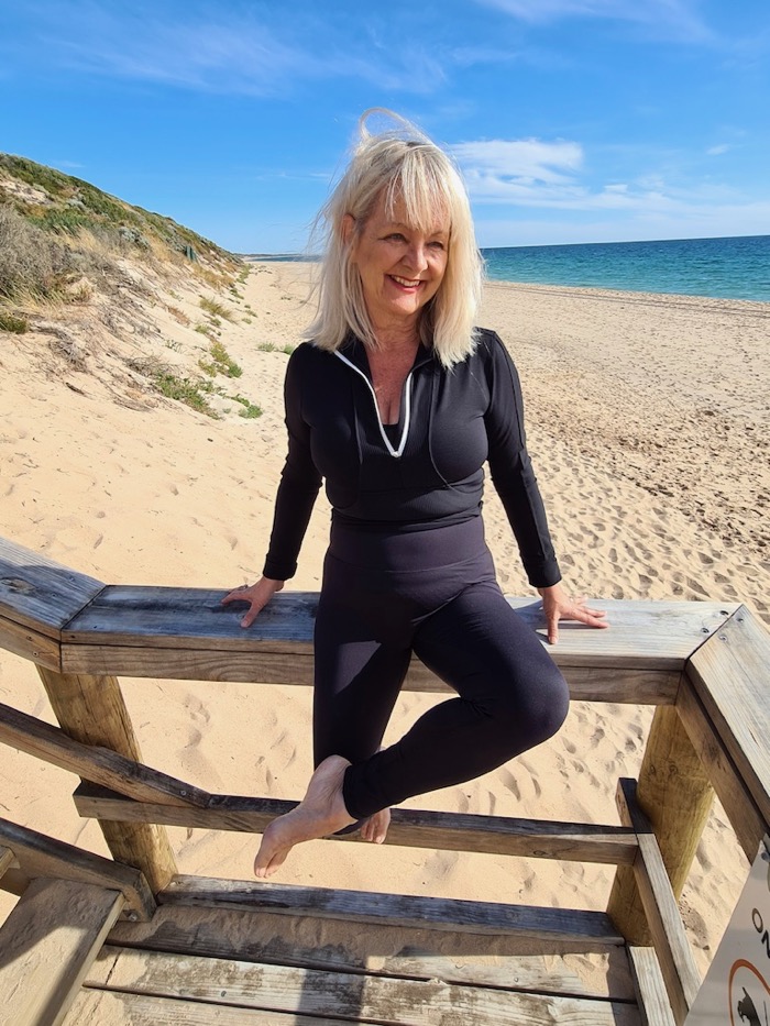 Woman sitting on wooden fence overlooking the ocean. She is wearing black yoga pants and top.