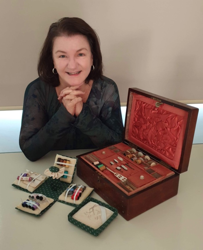 Sara from Learn Sewing Online an independent fashion designer creating the best organic clothing. She is sitting in front of an old sewing box and cotton threads.