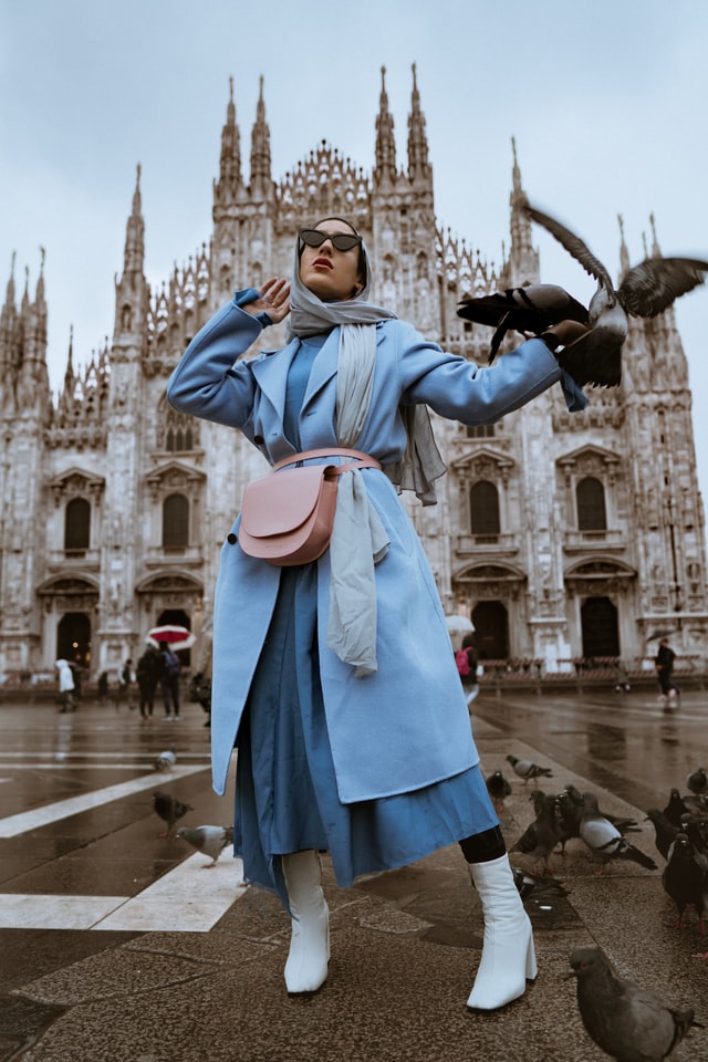 Woman wearing blue coat, blue dress and white ankle boots and blue scarf.