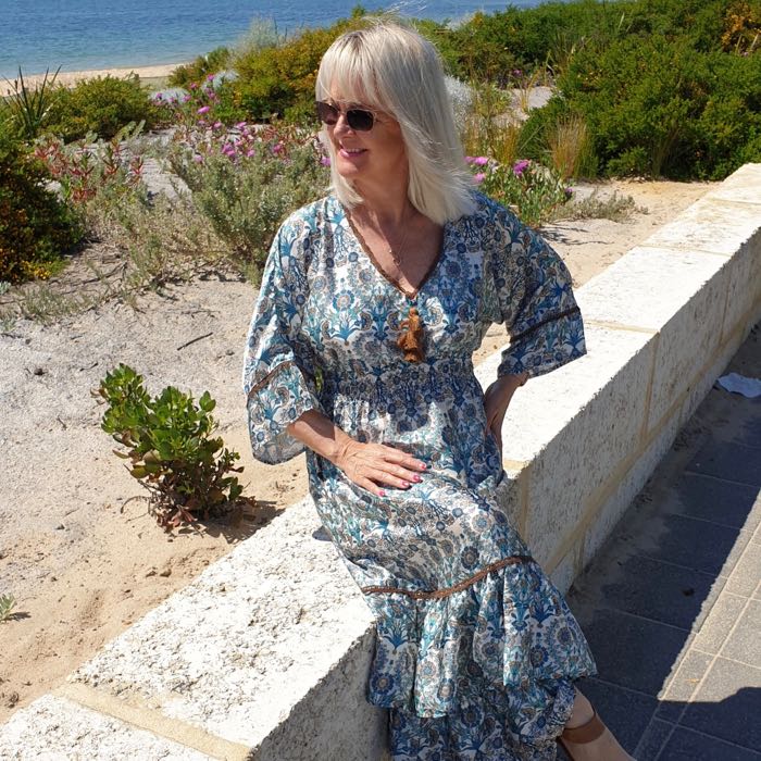 Woman sitting beside the sea. She is wearing sunglasses and a paisley print maxi dress.