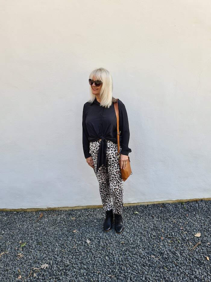 Blond woman wearing black technical blouse, dark glasses, animal print pants and black ankle post in a blog post outlining some sensational clothes for women over 50 years old.