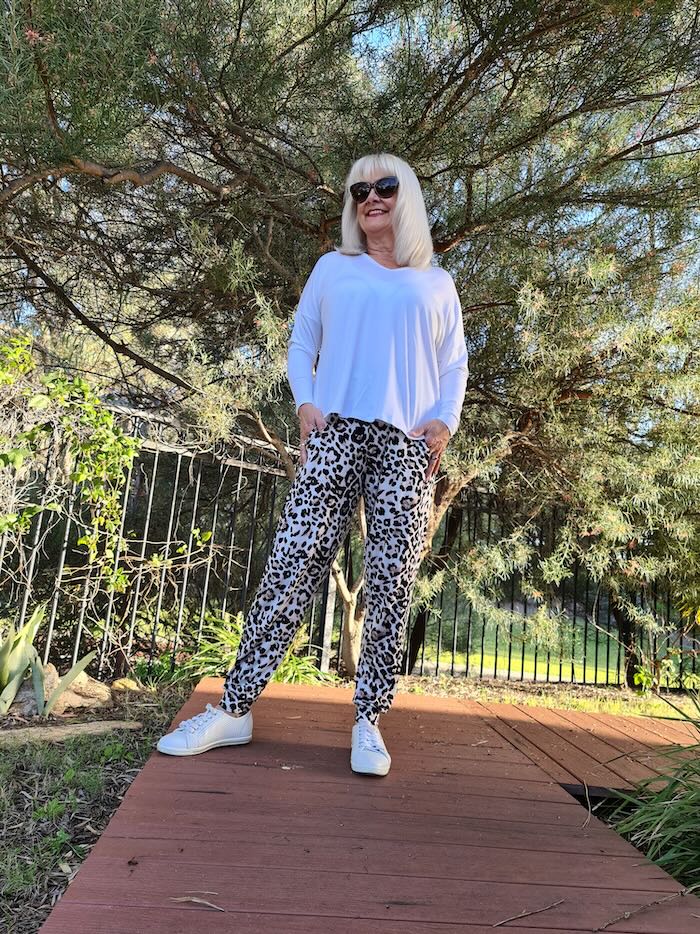 Blond woman over the age of 50 wearing sensational animal print pants and a camel top. On her feet she is wearing white sneakers.