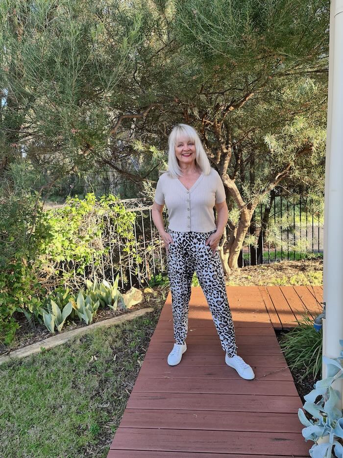 Blond woman over the age of 50 wearing sensational animal print pants and a camel top. On her feet she is wearing white sneakers.