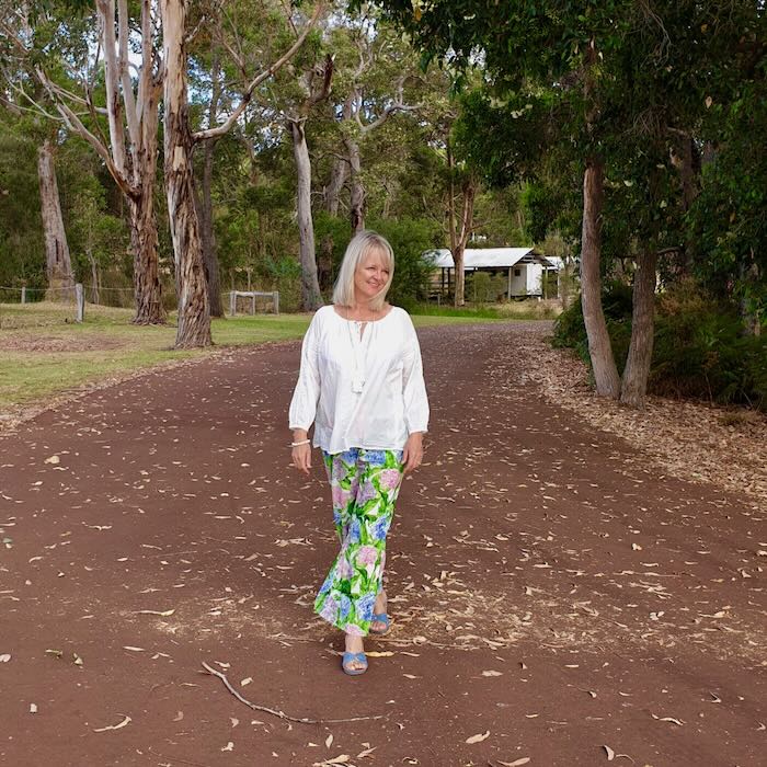 Woman wearing a white blouse and flower coloured cut off pants walking in a forest setting.