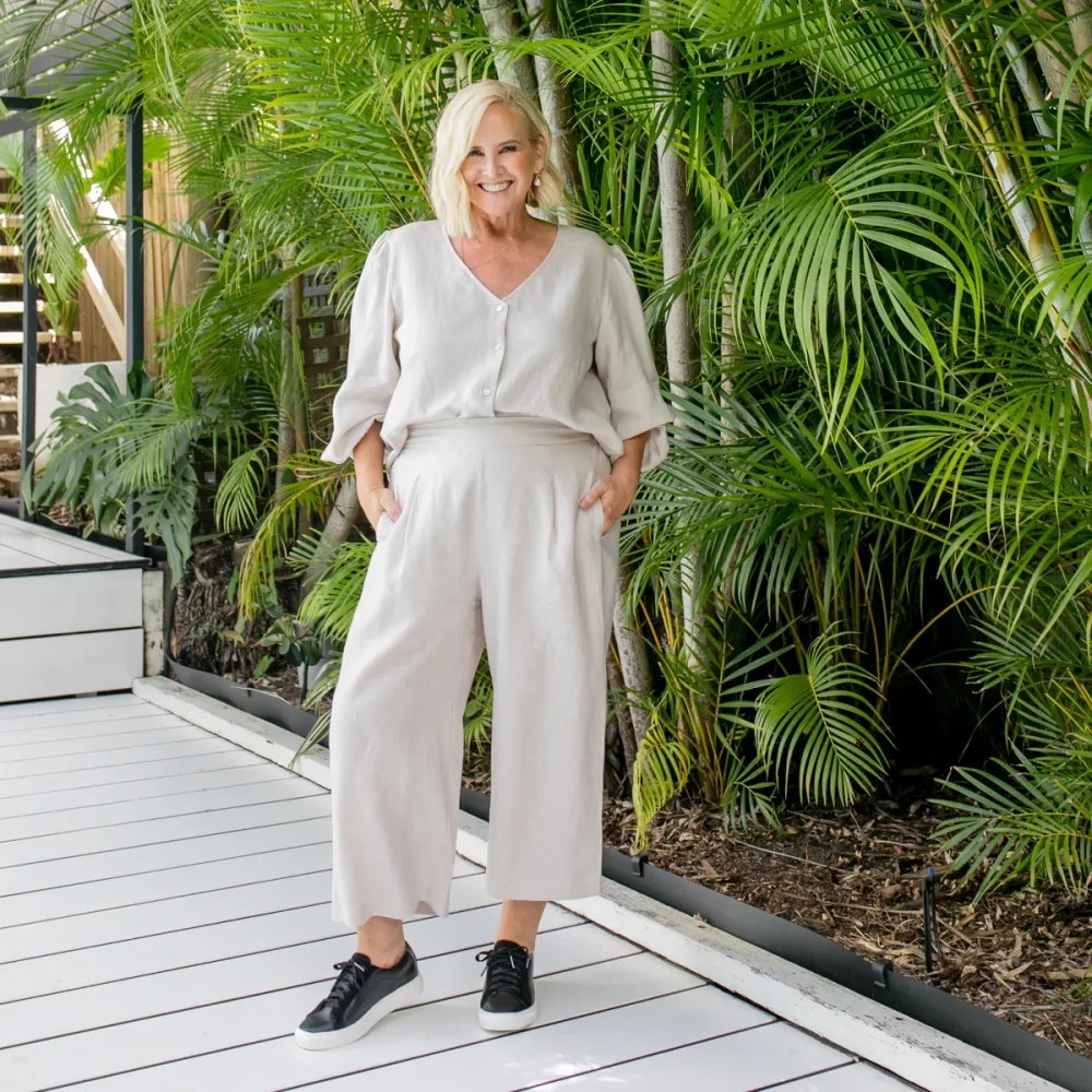 Blond woman wearing stone colored blouse and stone colored cropped pants, and black sneakers. 