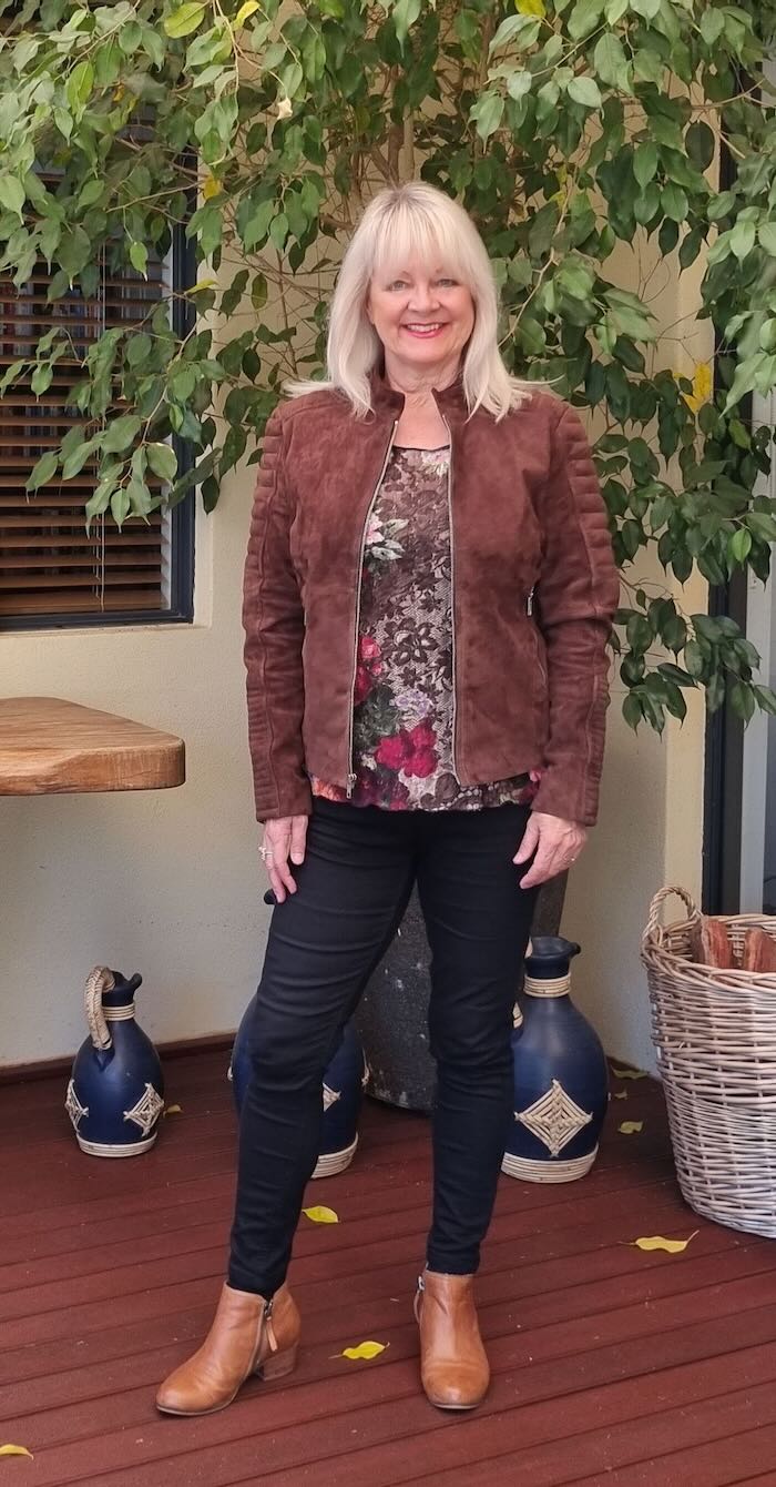 Woman wearing a suede leather jacket and a floral blouse with black skinny jeans.