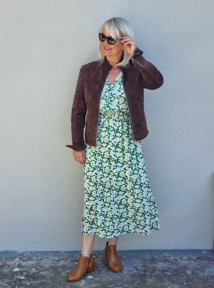 Woman wearing a green leaf print dress, and a leather jacket.