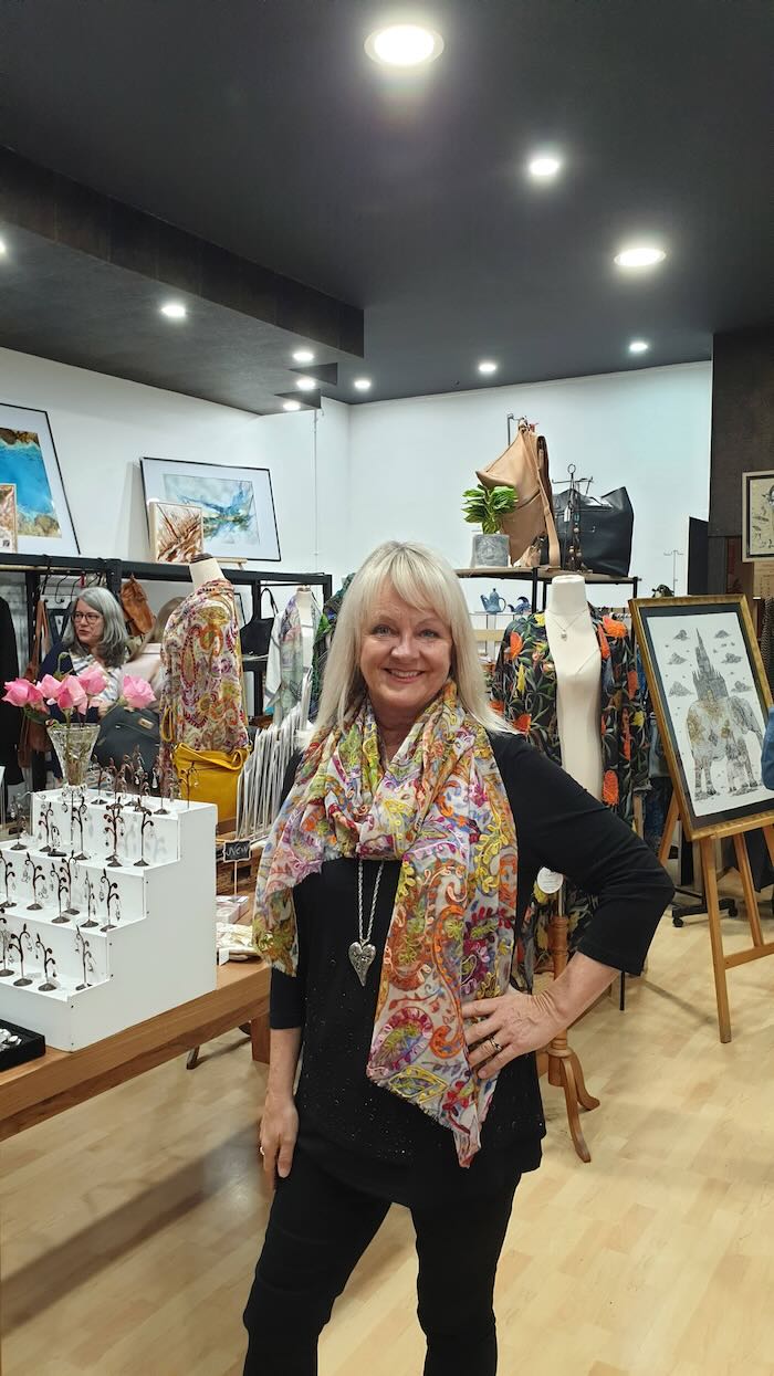 Woman in a boutique wearing black outfit and large brocade scarf.