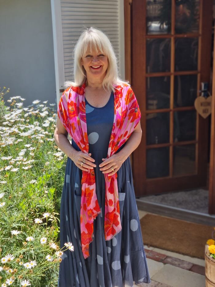 Blond woman wearing a spotty print navy summer dress and a bright pink scarf over her shoulders.