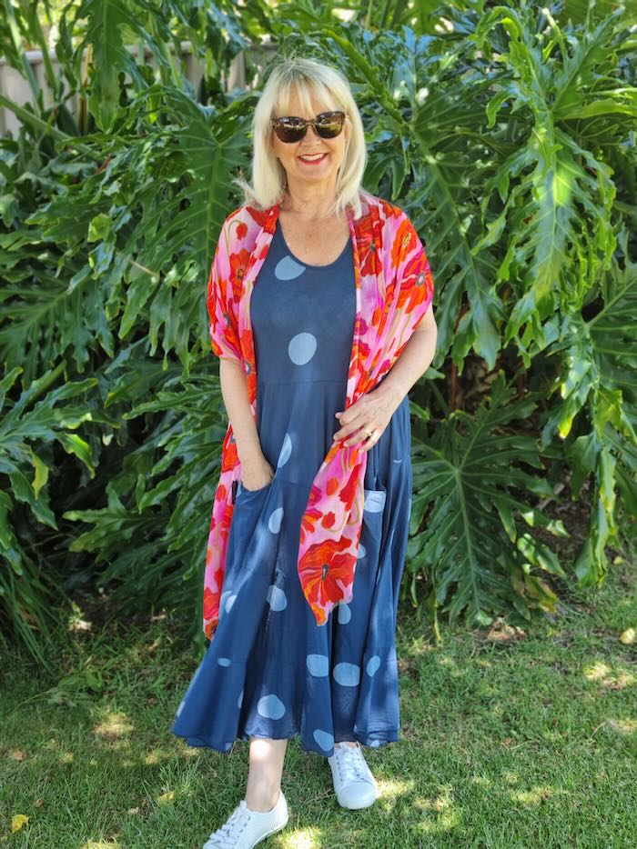 Blond woman wearing a soft linen, spotty summer dress in blue, with a red and orange scarf.