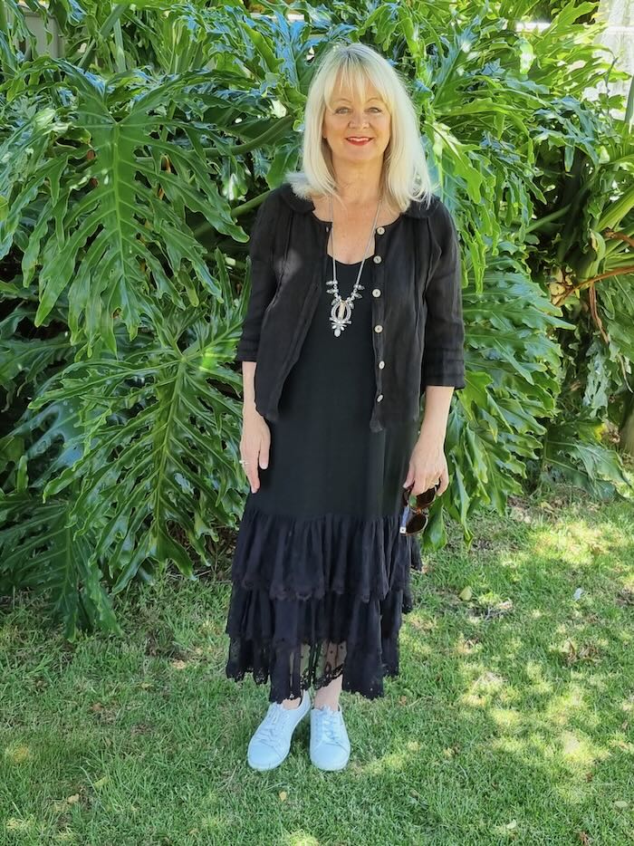 Blond woman over 50 wearing a black summer dress and linen jacket