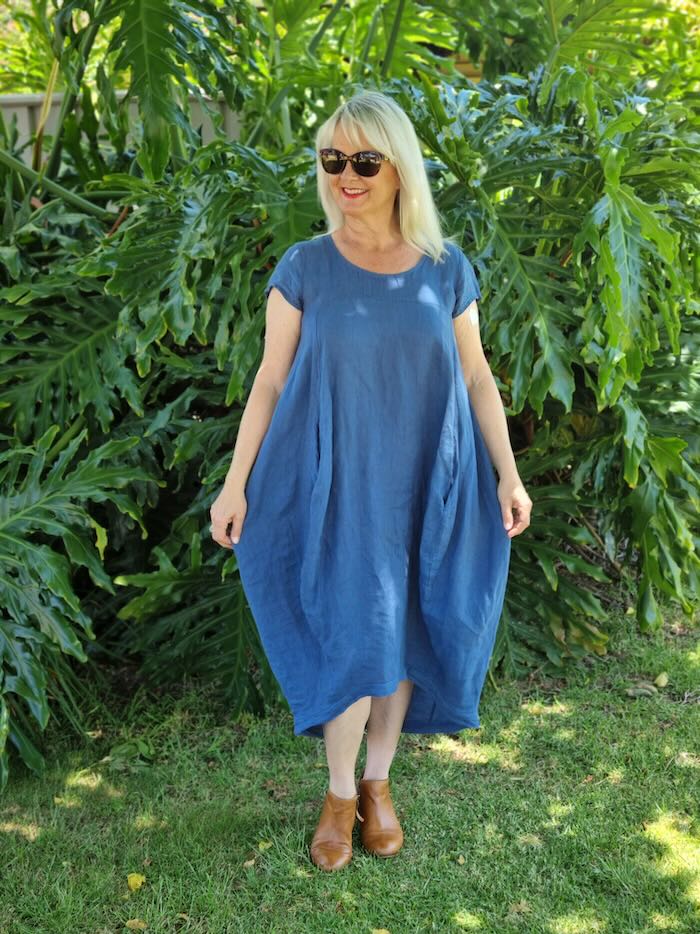 Blond woman over the age of 50 wearing a blue linen summer dress.