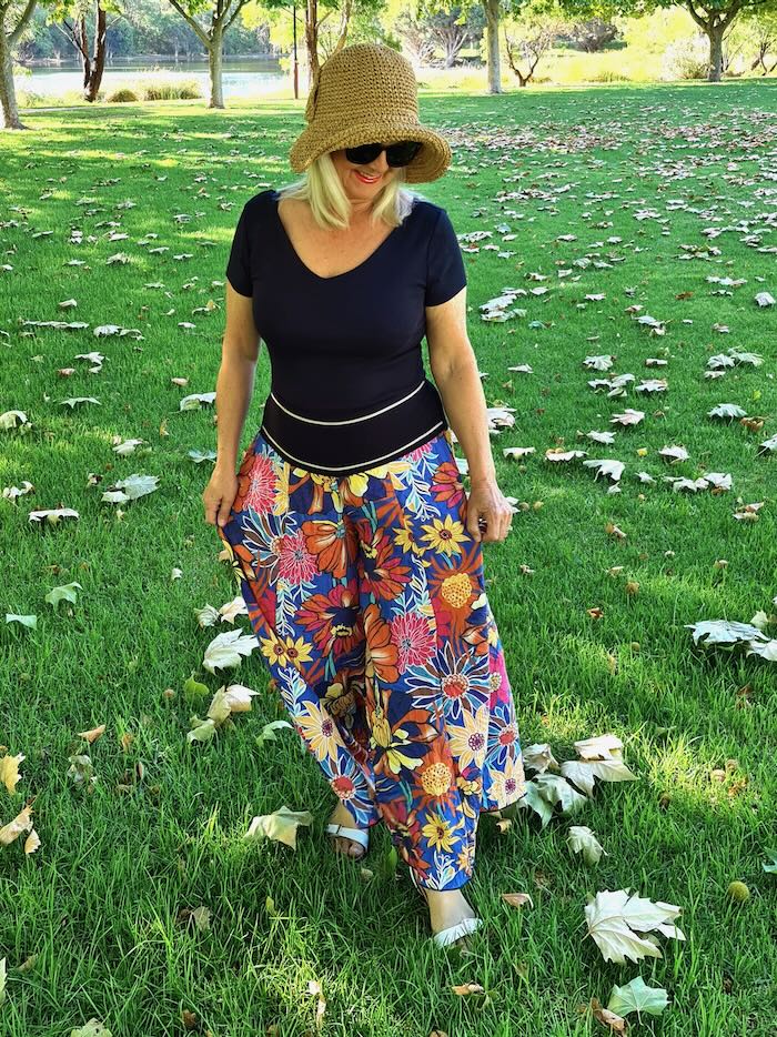 Lady wearing straw hat, black top and flowery wide leg pants. She is illustrating a point in the blog post about wearing wide leg pants over 50.