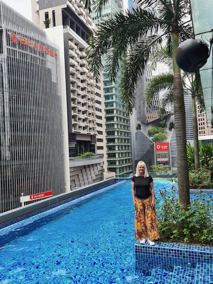 Woman by a swimming pool, amid high rise buildings in Singapore, wearing wide leg pants and a black top illustrating, what is a Bohemian look?