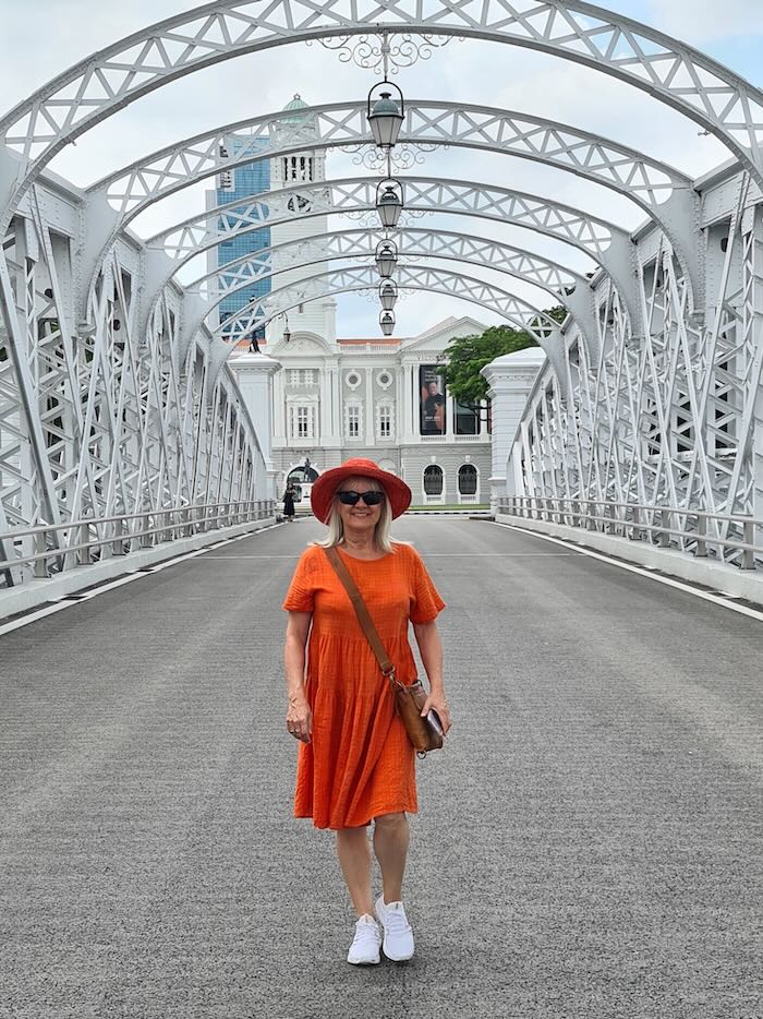 This image illustrates how to wear Bohemian dresses. Woman is wearing an orange dress, orange floppy hat, big dark sunglasses, leather handbag and sneakers.