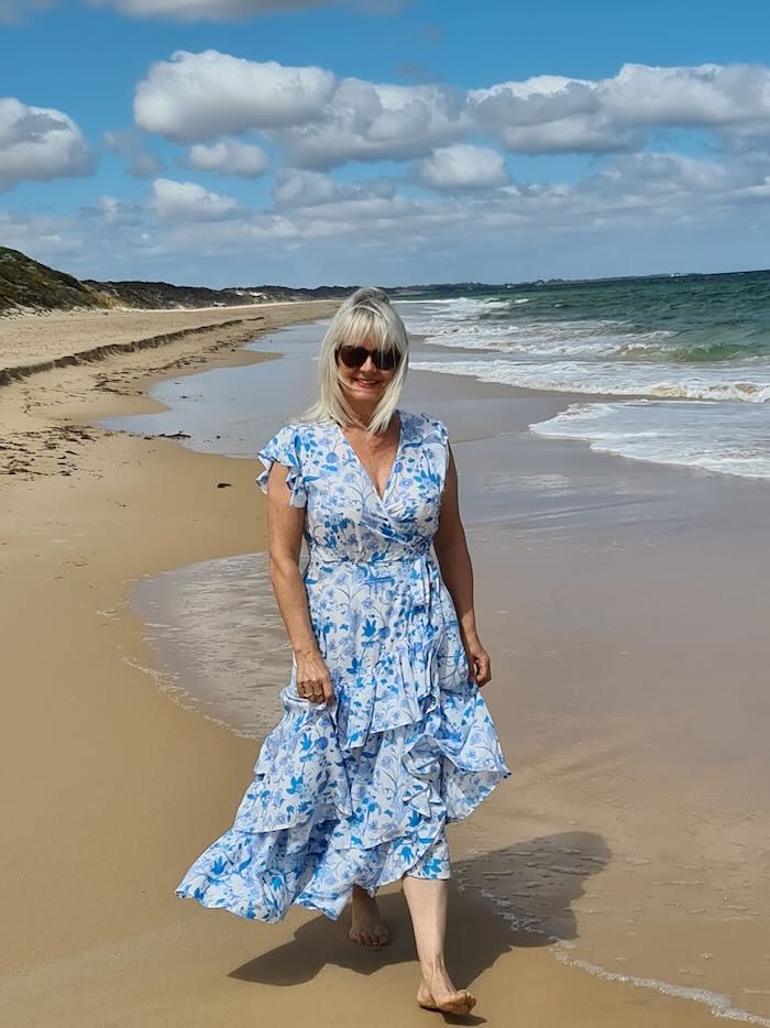 Woman wearing wrap boho style dress walking on a beach. Illustrating a point about some of the Best Boho Dress Styles for Older Women.