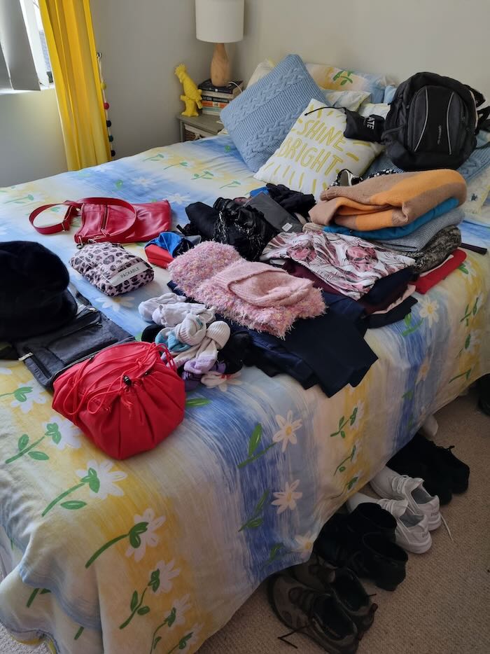 Packing list for Alaska cruise, image shows a bed piled with folded clothes and accessories suitable as casual wear for a cruise to Alaska.