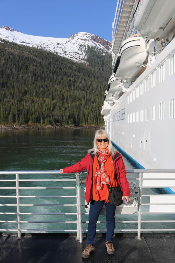 Woman standing by a ship wearing birght orange and red colored, warm layers suitable for an Alaska Cruise