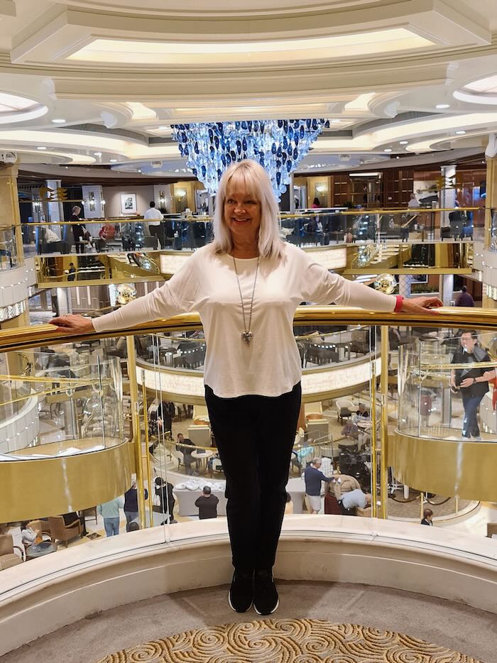 Woman standing on staircase of cruise ship wearing white Tee and black pants.