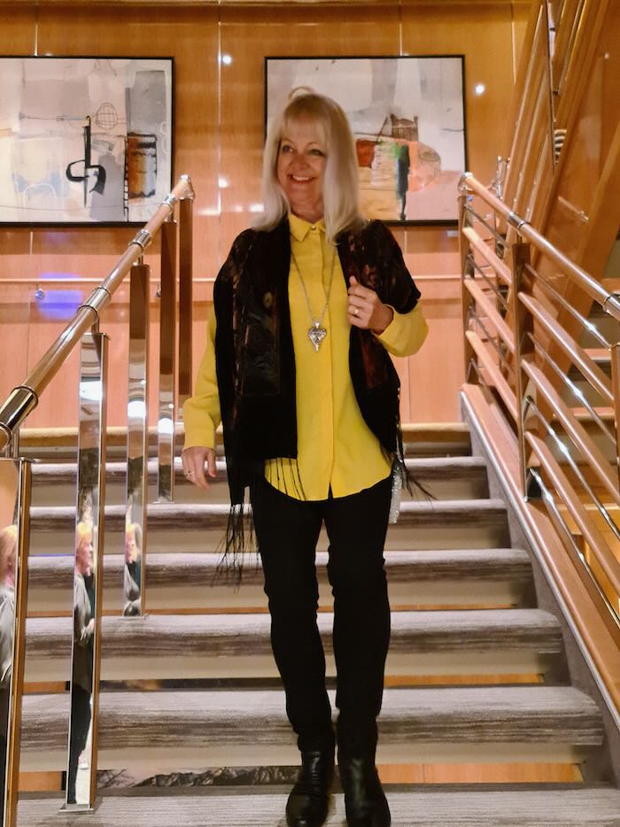 Woman on a cruise ship in Alaska wearing a yellow long sleeve blouse, black pants and a black shawl.