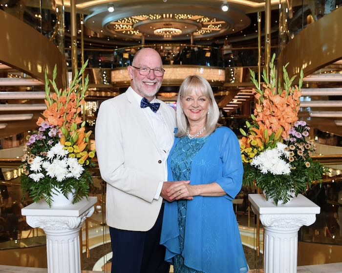 Elderly man and mature age blond woman wearing formal clothes suitable to wear on a cruise to Alaska. He is wearing a jacket and bow tie, she is wearing a blue cocktail dress.