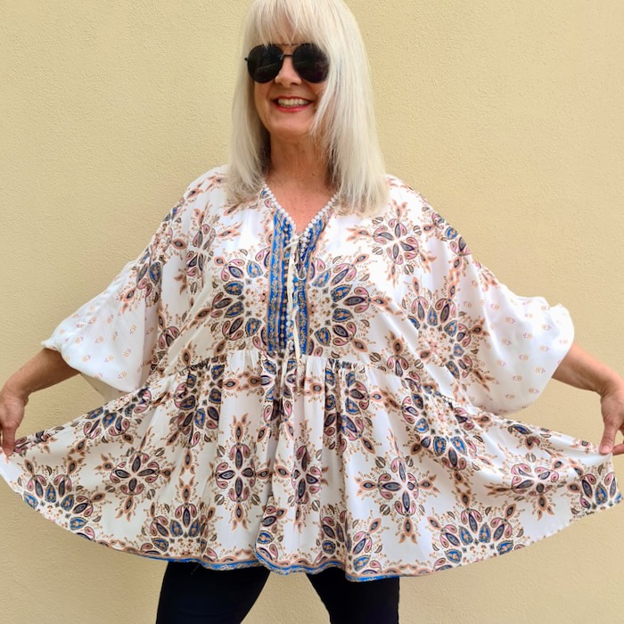 Blond haired woman wearing dark sunglasses and a gemstone, floral print, floaty blouse. She is illustrating a bohemian inspired outfit.