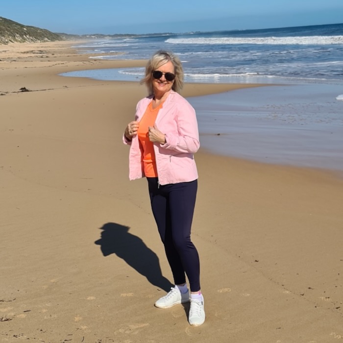 Woman on the beach wearing a pink top and navy blue activewear, tummy control leggings.