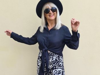 Woman wearing black blouse and floral print black pants and a black wide brimmed hat, illustrating boho chic outfits.