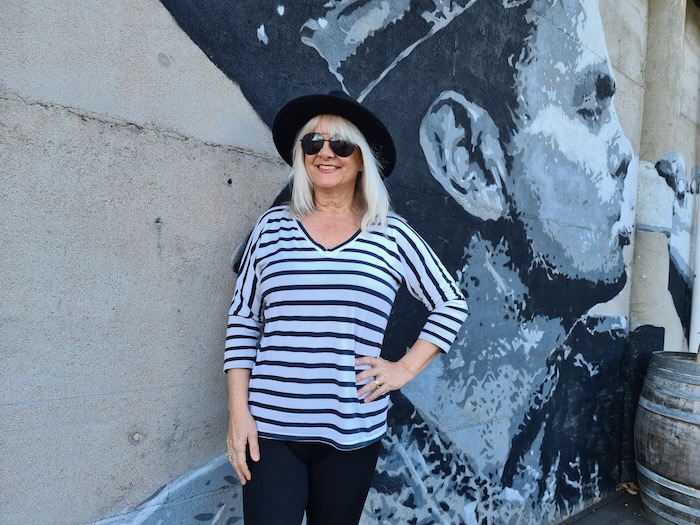 Woman wearing black hat and black and white stripey blouse with black trousers.