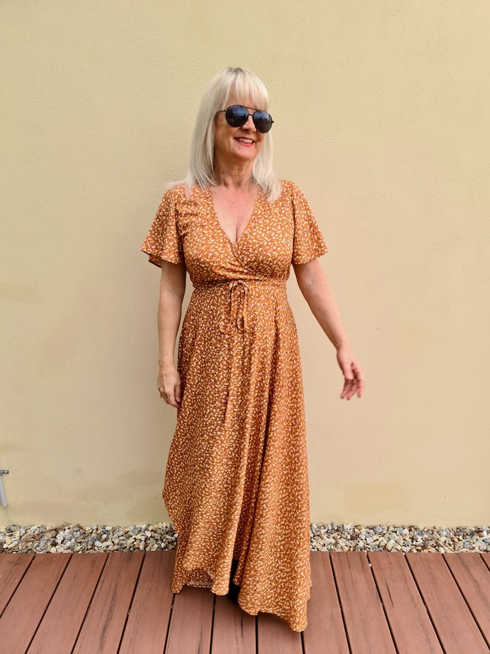 Blond lady smiling. She is wearing a rust colored maxi, wrap dress.
