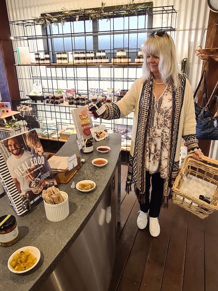 Woman browsing in a gift shop. She is illustrating what to wear if you're petite and curvy. She's wearing a Pasadena tassle cardigan, gemstone print top, black slimline pants and white sneakers.