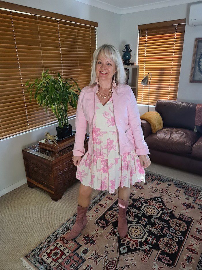 Woman showing how to wear summer dresses in winter. She is wearing a pinnk and white summer mini dress which she has layered with a jacket, tights and pink suede boots.