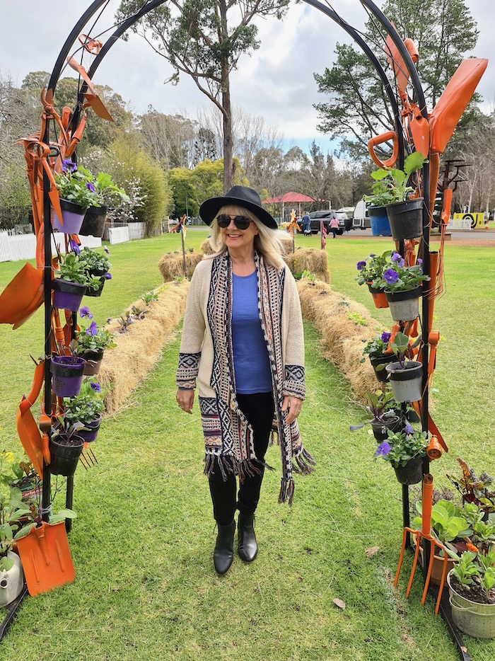 Woman walking in a field under an archway. She's wearing a long line cardigan, flowy top and black pants illustrating clothes suitable for short and curvy women.