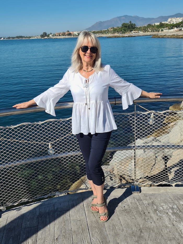 Jo wearing the white Sandy top on vacation. She is standing by the ocean.