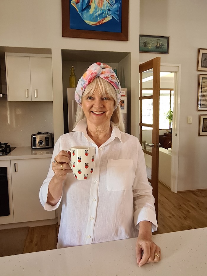 Woman wearing a white shirt standing in a kitchen drinking a cup of coffee