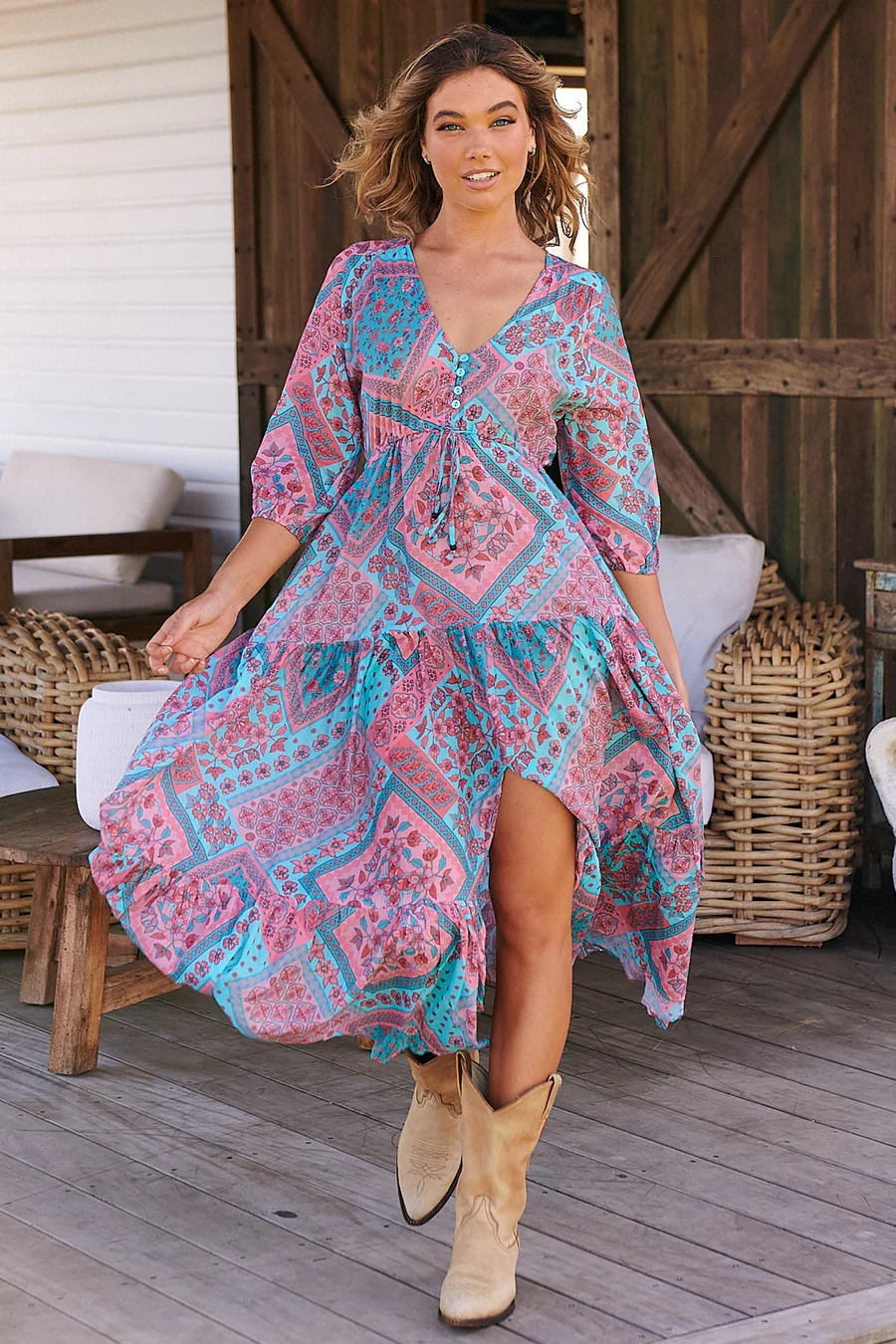 Model wearing a boho maxi dress suitable for women over 50. Dress is pink and blue. Her cowboy boots are in camel color.