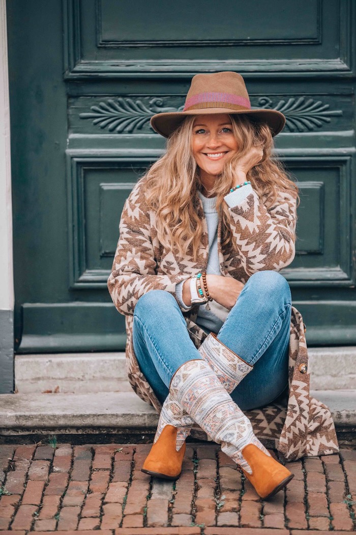 Blond woman sitting cross legged by a door wearing boho clothes.