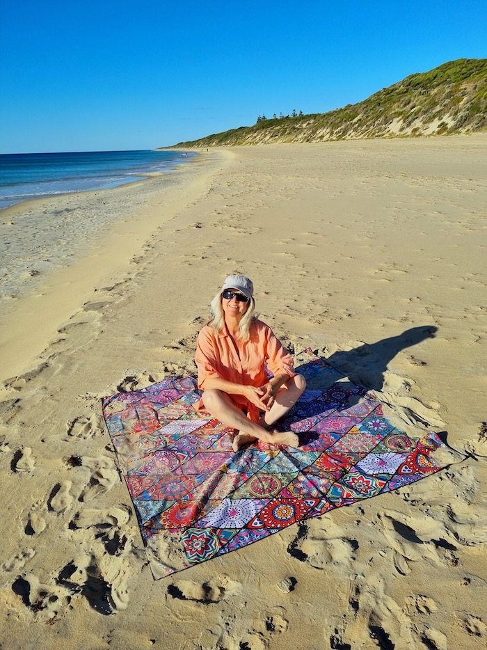 Woman sitting on a sand free beach towel on a lonely stretch of beach.
