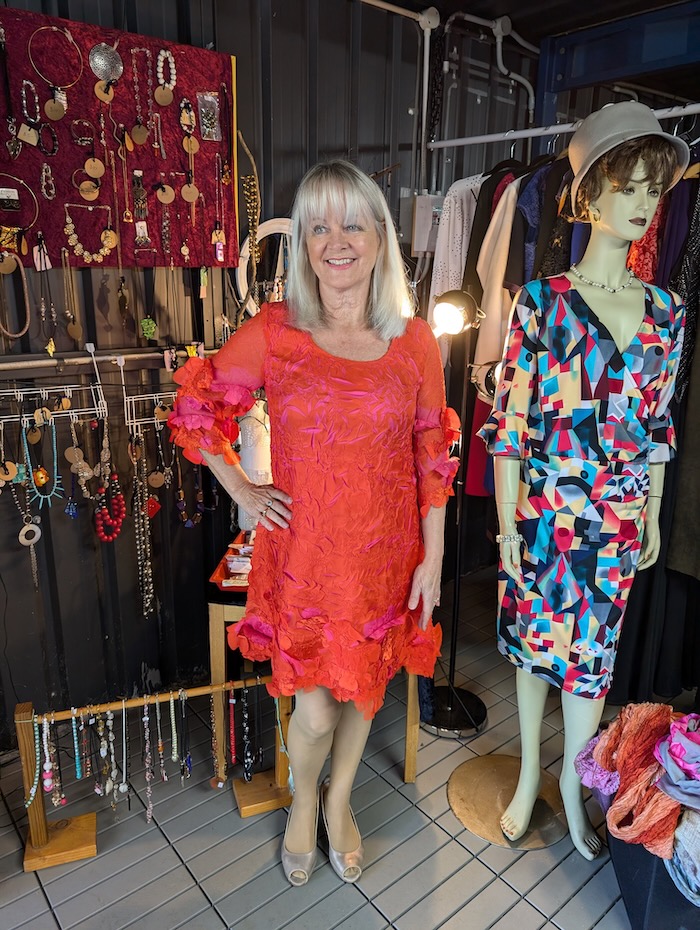 Woman wearing a bright red dress. She is standing in a charity shop.