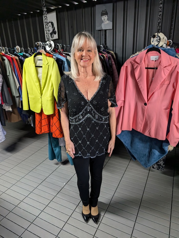 Woman wearing a black outfit. She is standing in a charity shop.